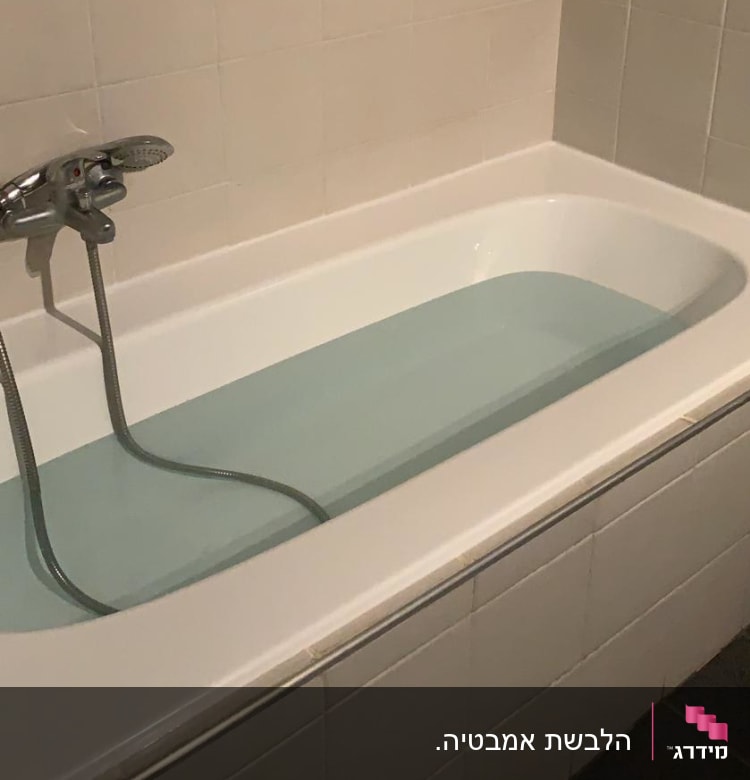 אמבטיה עם מים וברז מתכת על קיר מרוצף